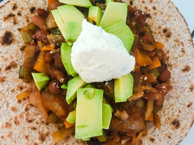 Tostasda topped with mixed beans, avocado, sprinkling of cheese and a spoonful of sour cream